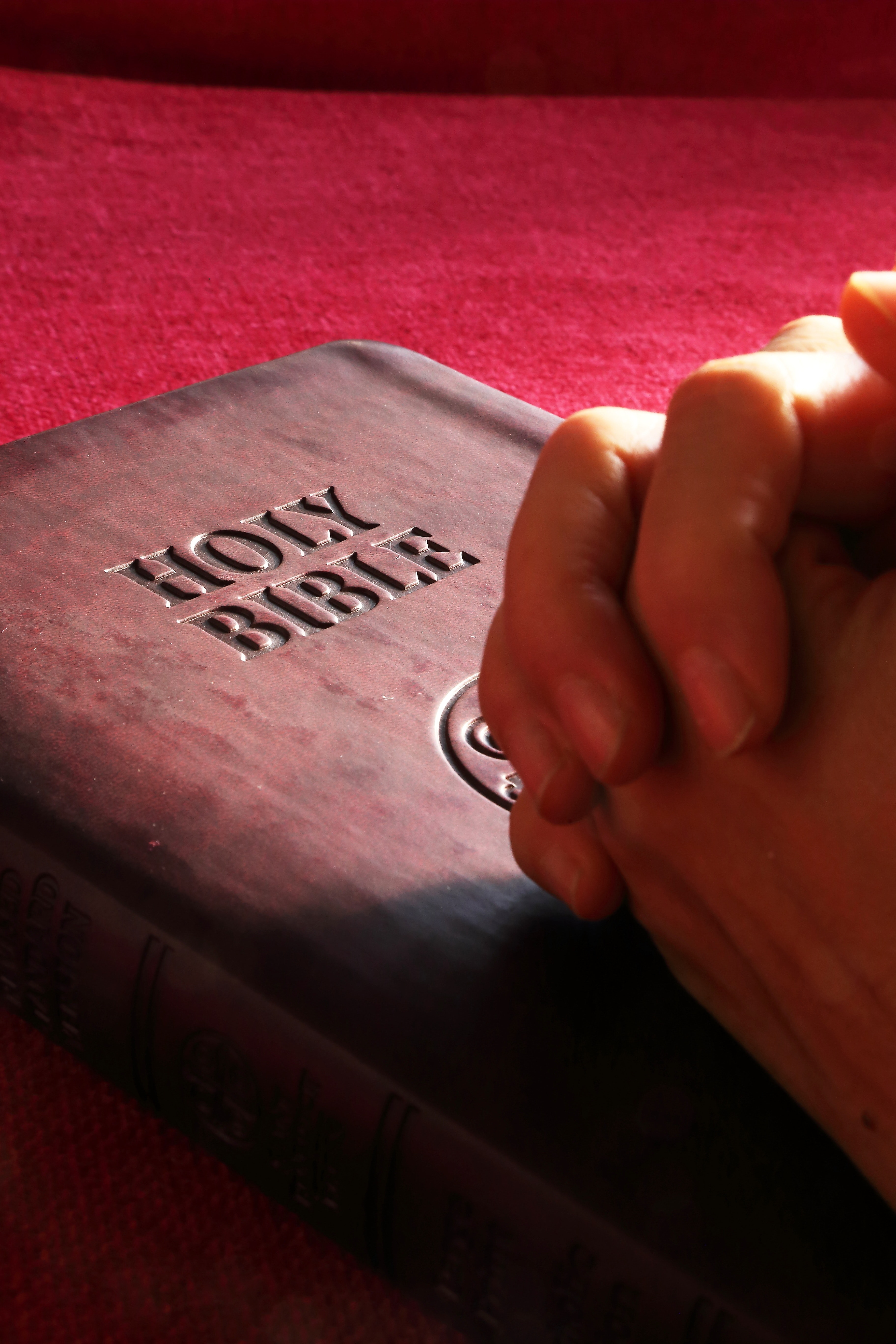 Bible with folded hands in prayer on top.